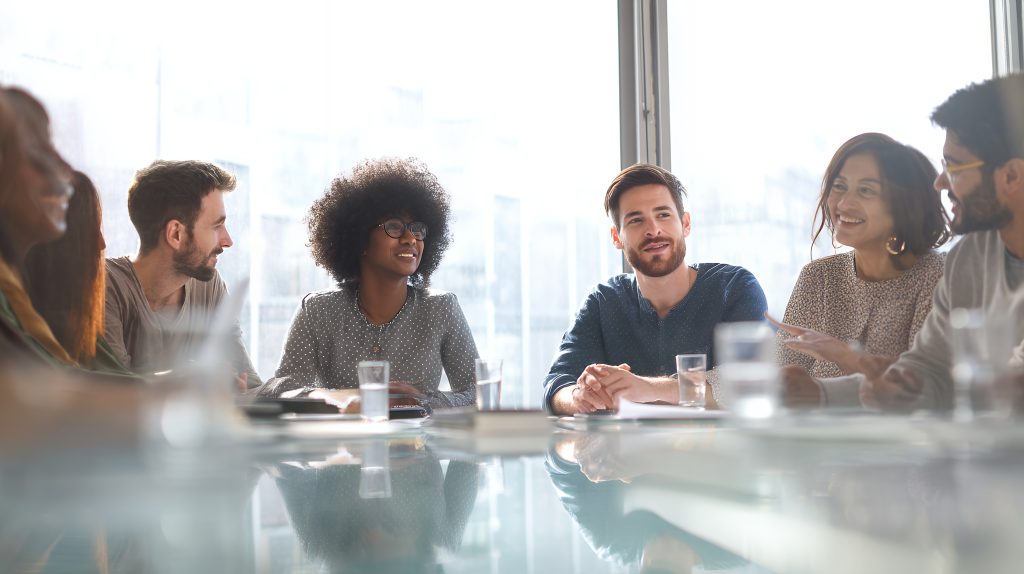 Grupo de profesionales en una reunión de equipo colaborativa, sonriendo y interactuando, ilustrando la aplicación de la psicología positiva en el entorno laboral.